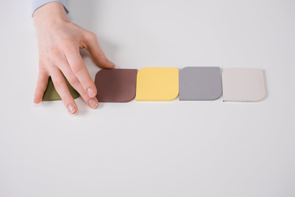 A close-up of a hand arranging colorful tiles on a white table, showcasing pastel tones.